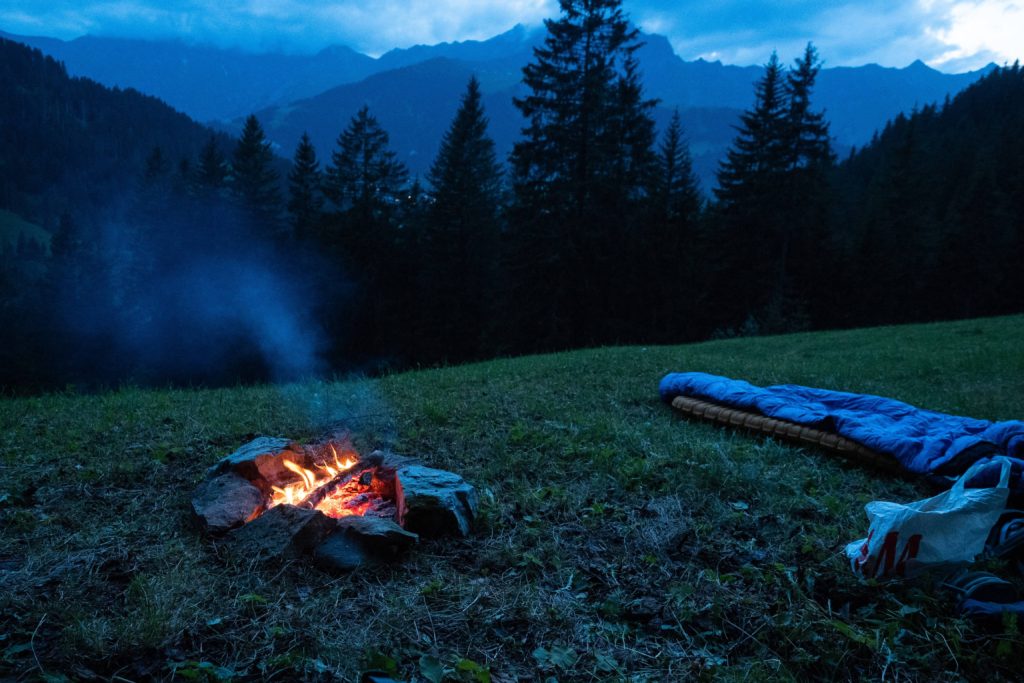 A photograph of a sleeping bag by a campfire in the mountain setting.