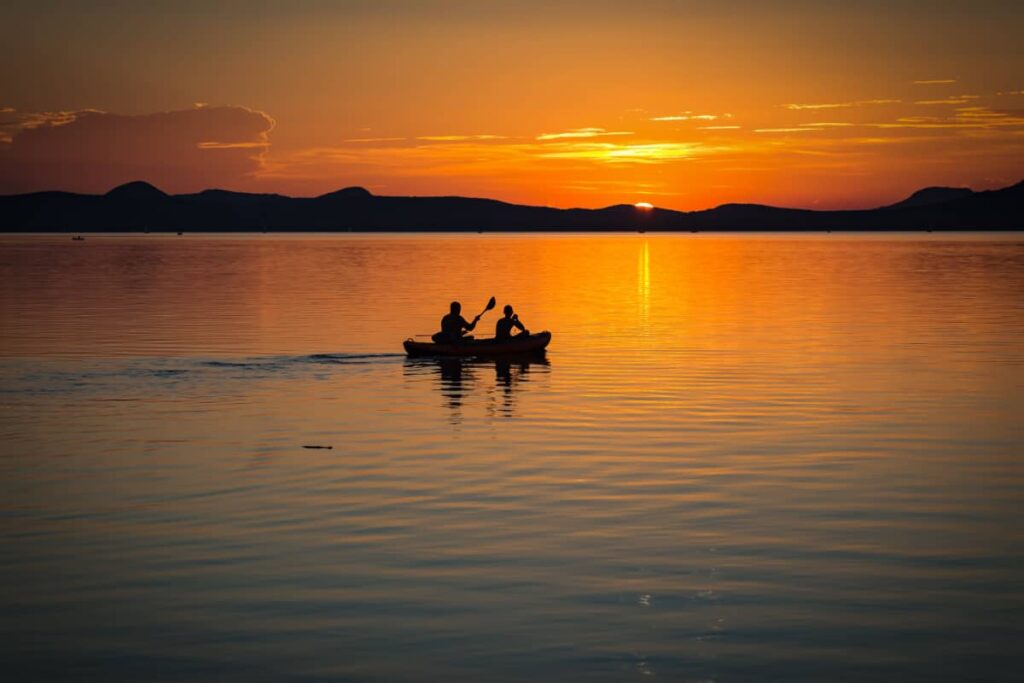 a photo of a canoe on the lake with two people at sunset