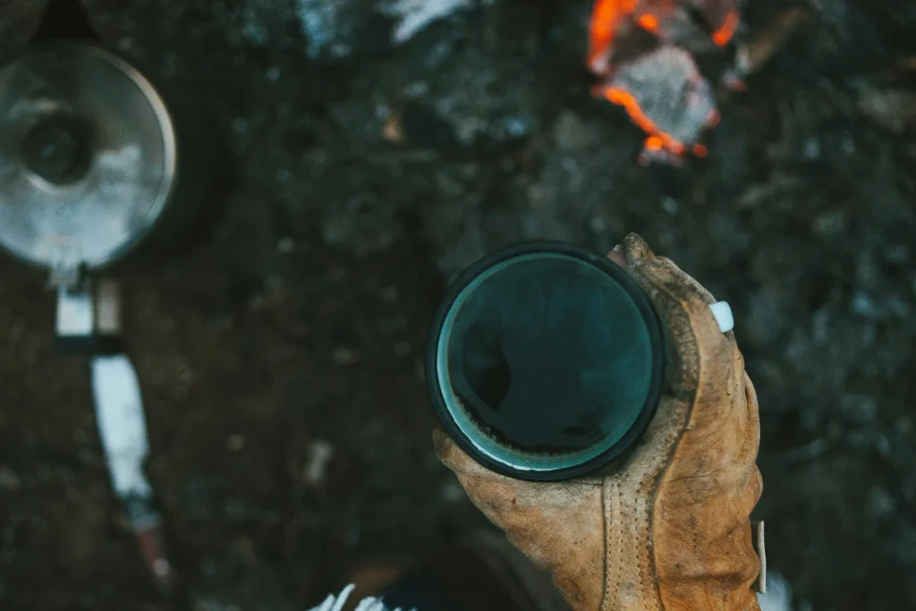 a cup of cowboy coffee with a pot and campfire in the background.